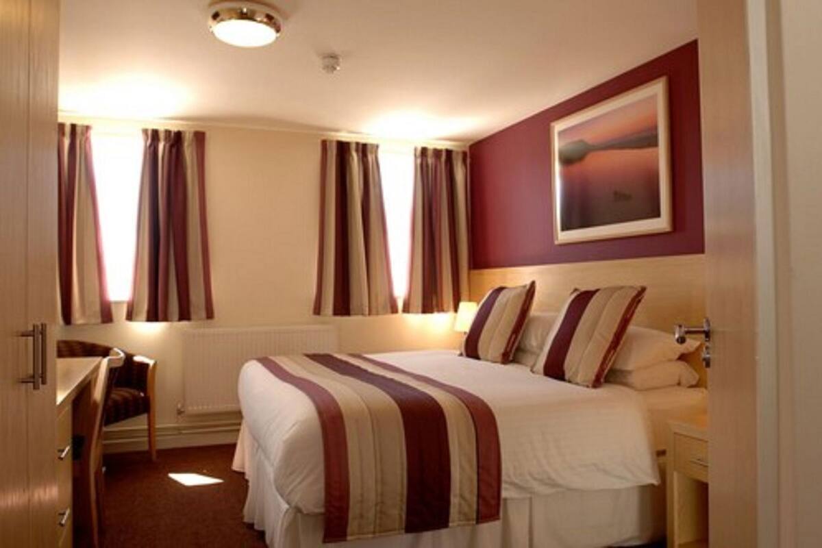 A hotel room with a bed, a desk, and a window with curtains.