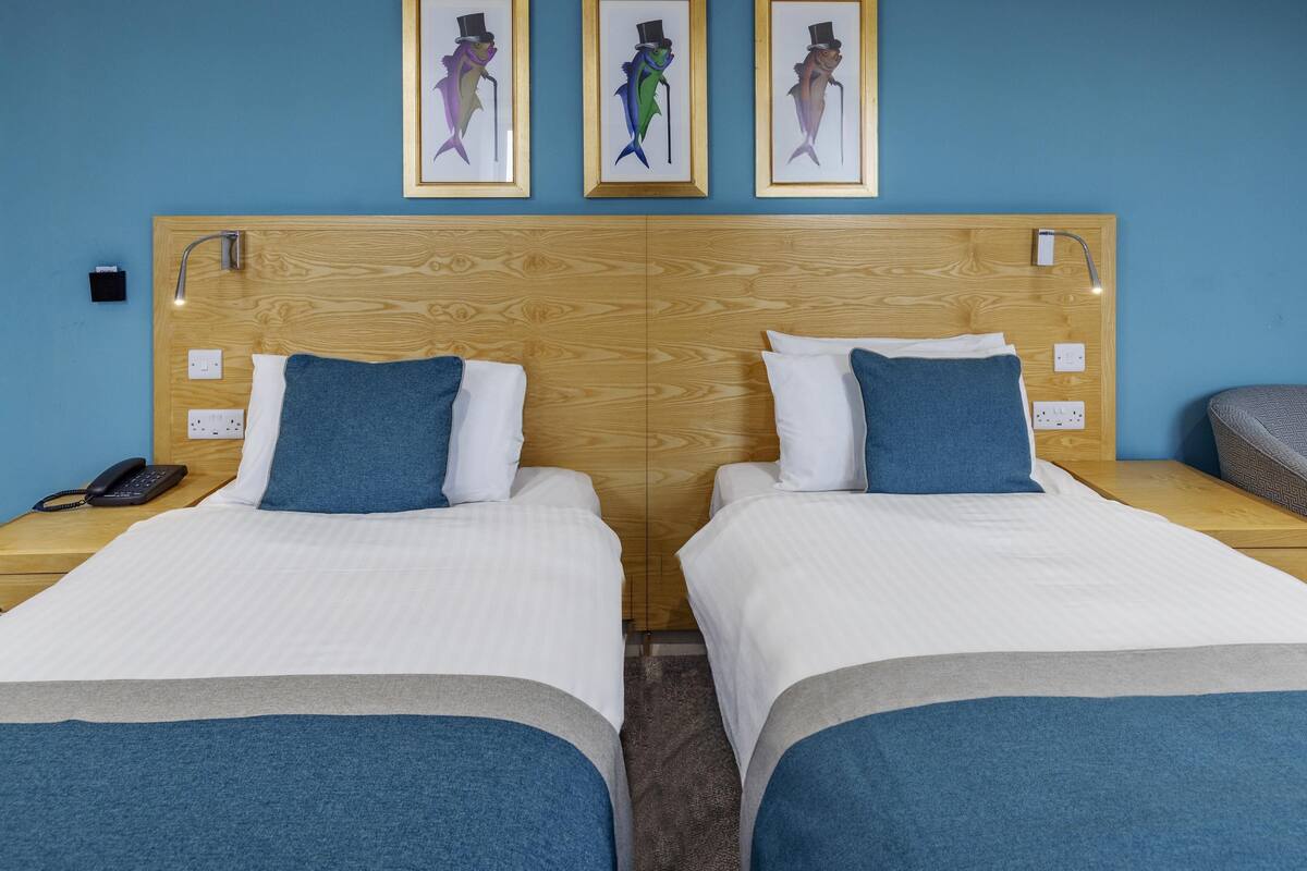A double room with two beds, a wooden headboard, a phone on the nightstand, and framed artwork on the wall.