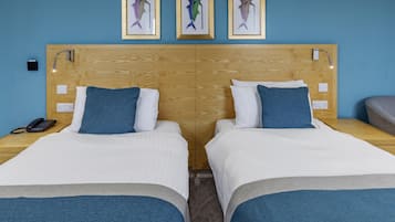 Een tweepersoonskamer met twee bedden, een houten hoofdeinde, een telefoon op het nachtkastje en lijstjes met kunstwerken aan de muur.