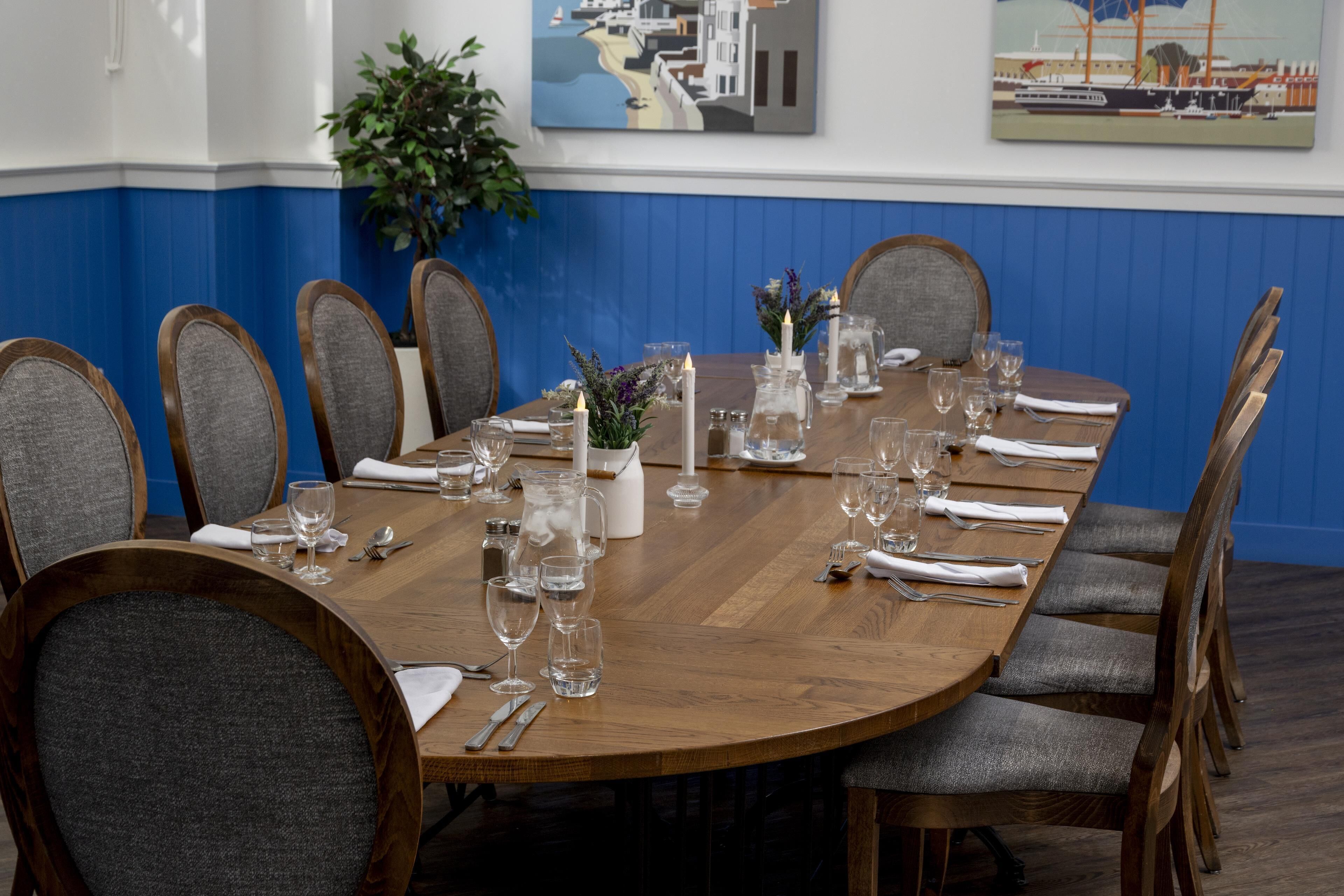 A dining table set for eight with chairs, candles, and a vase of flowers.