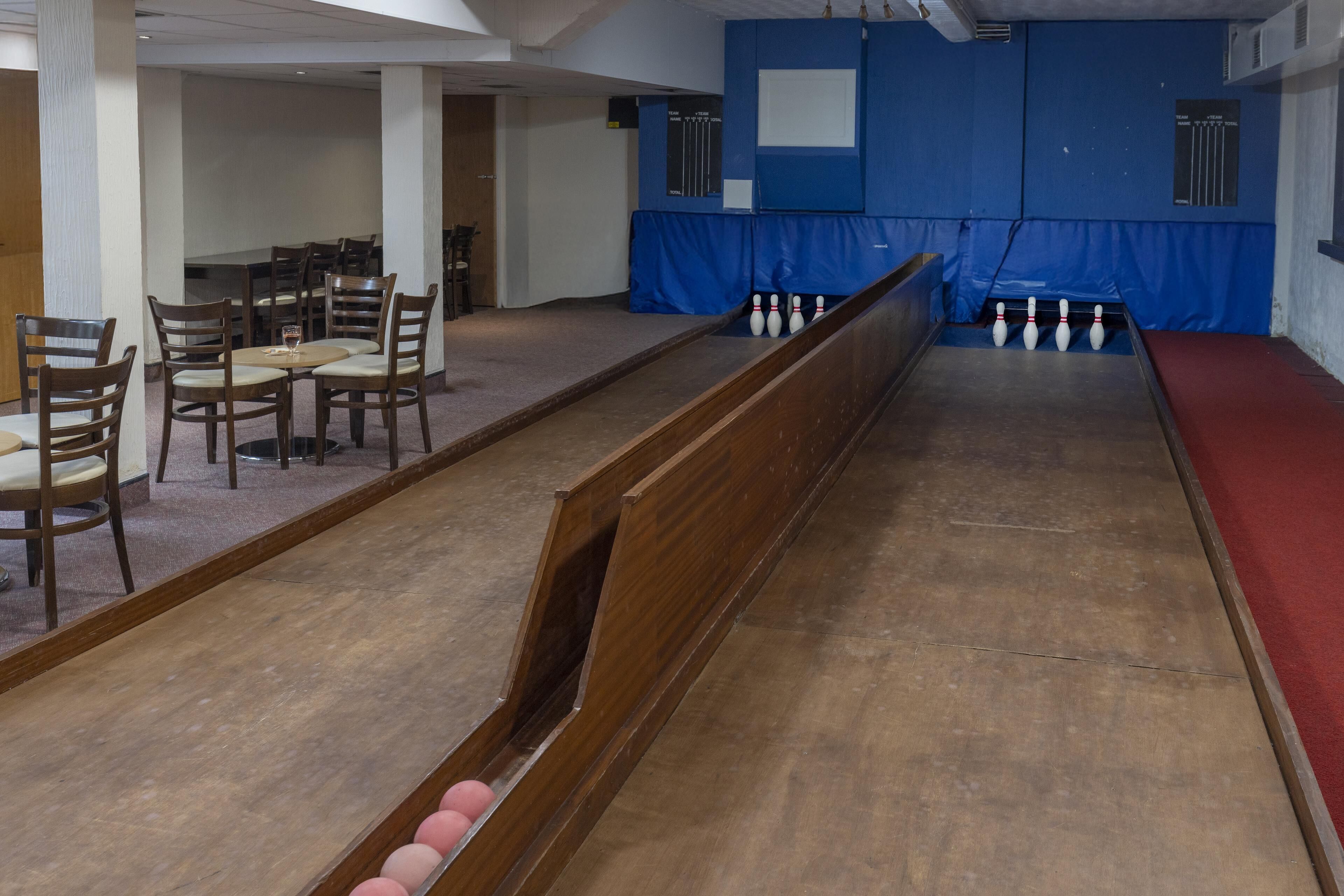 A bowling alley with wooden lanes, a red seating area, and a blue padded wall.