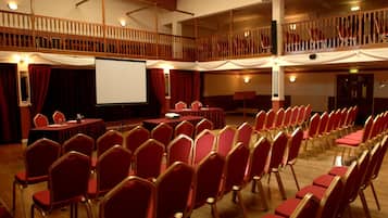 Un salón de conferencias con asientos escalonados, un escenario con pantalla y un balcón.