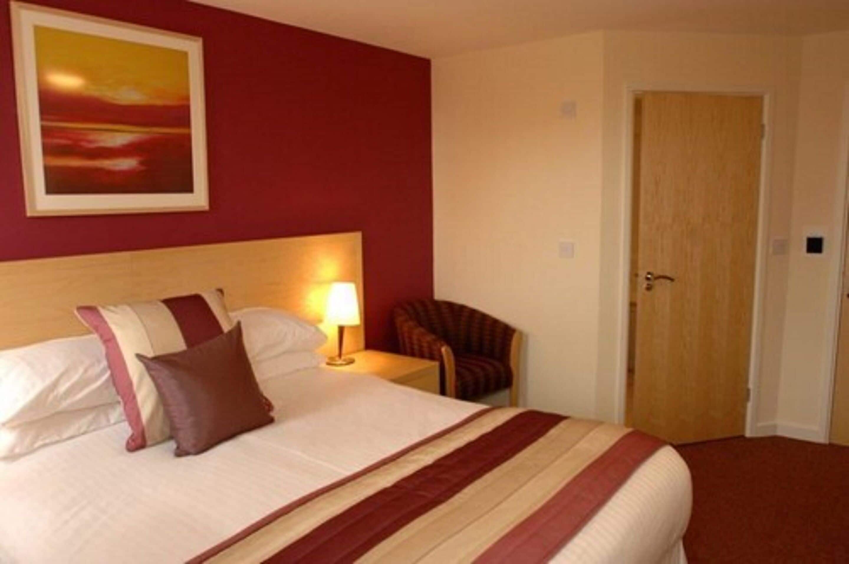 Habitación de hotel con cama, mesita de noche, silla y puerta.