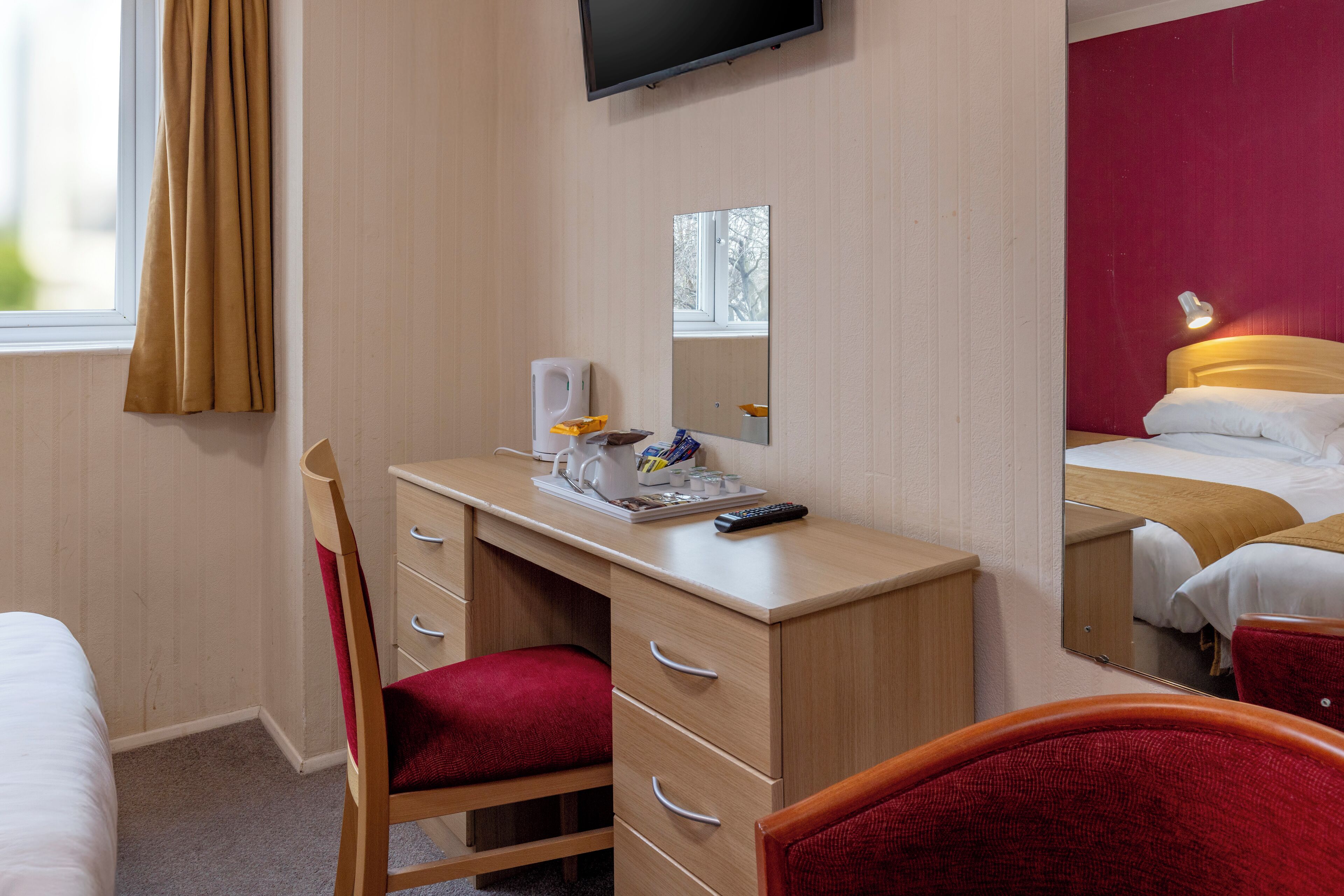 A hotel room with a desk, chair, bed, and a television.