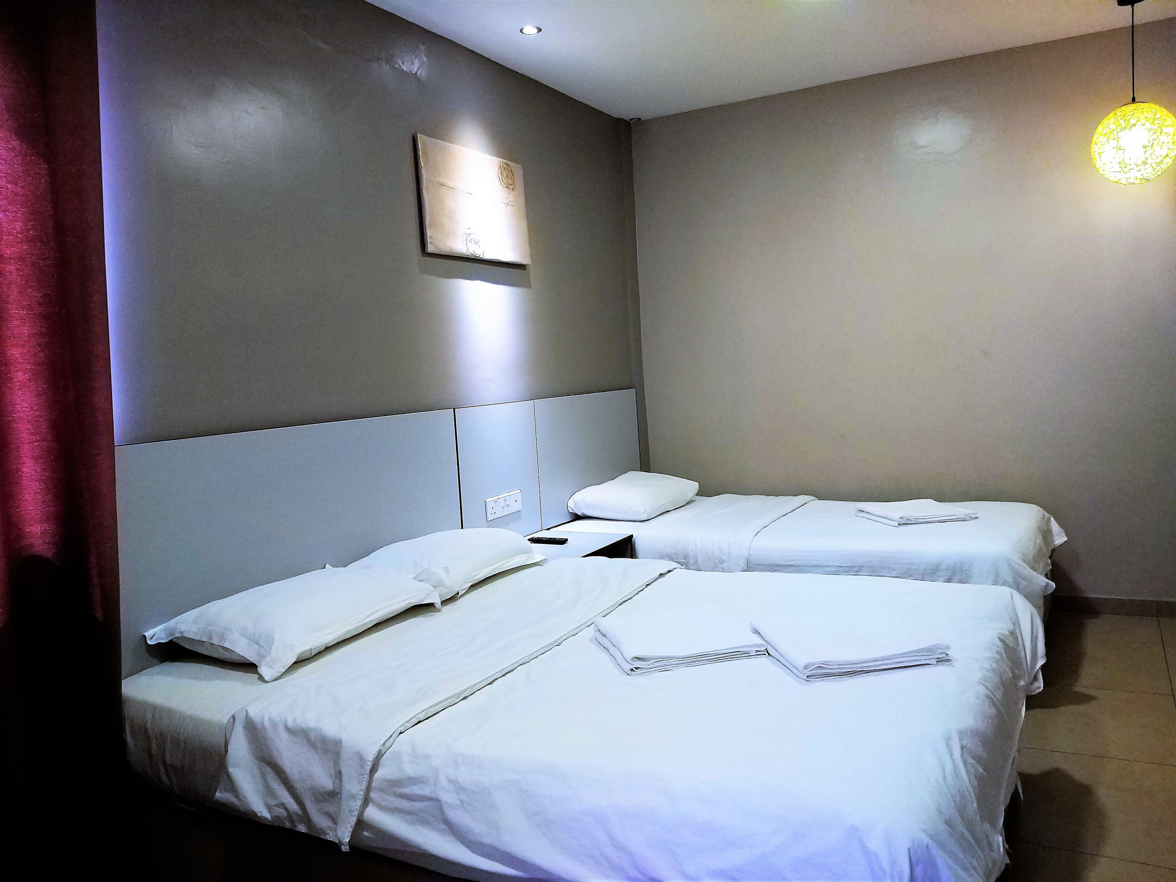 A hotel room with two beds, each with white bedding and pillows, a headboard, and a wall-mounted light fixture.