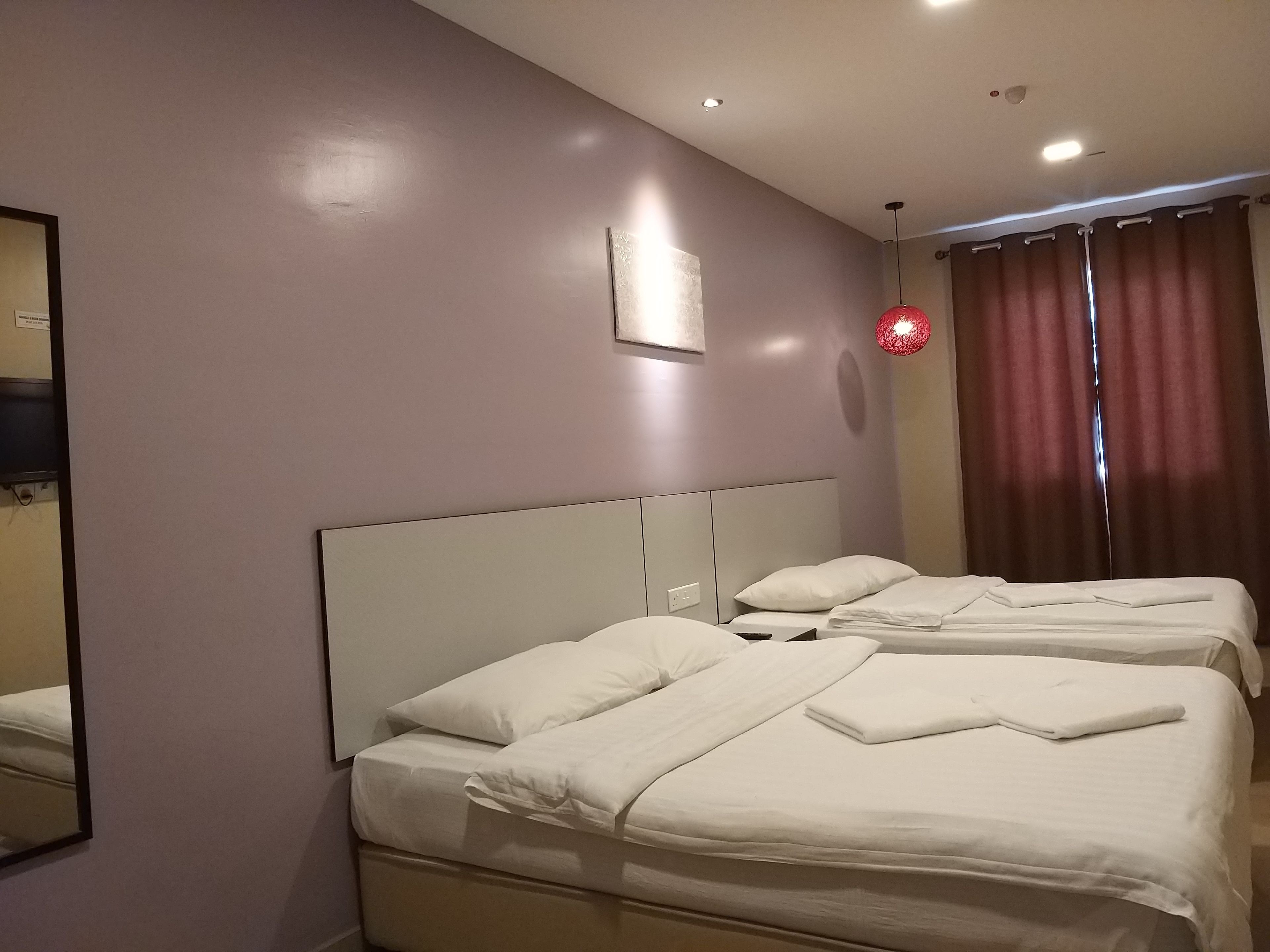 Een hotelkamer met twee bedden, een grote spiegel en een rode hanglamp.