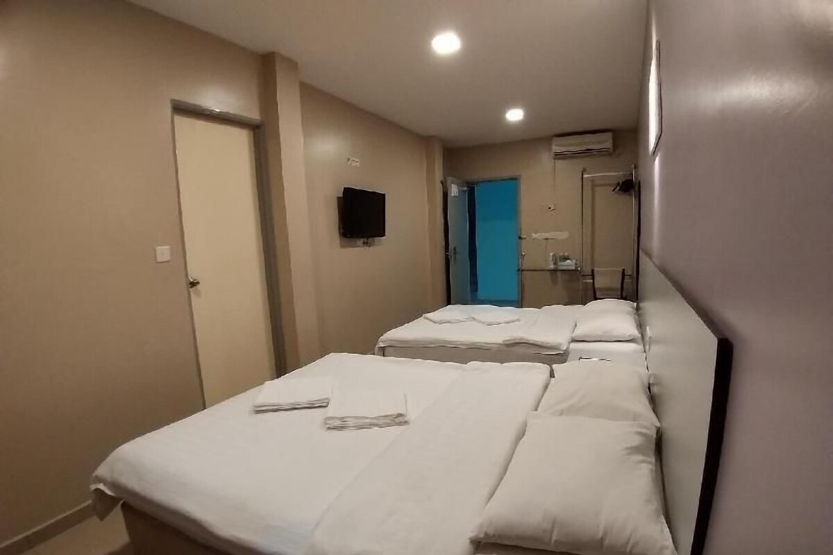 Ein Hotelzimmer mit zwei Betten, einem Fernseher, einer Tür und einem durch eine offene Tür erreichbaren Badezimmer.