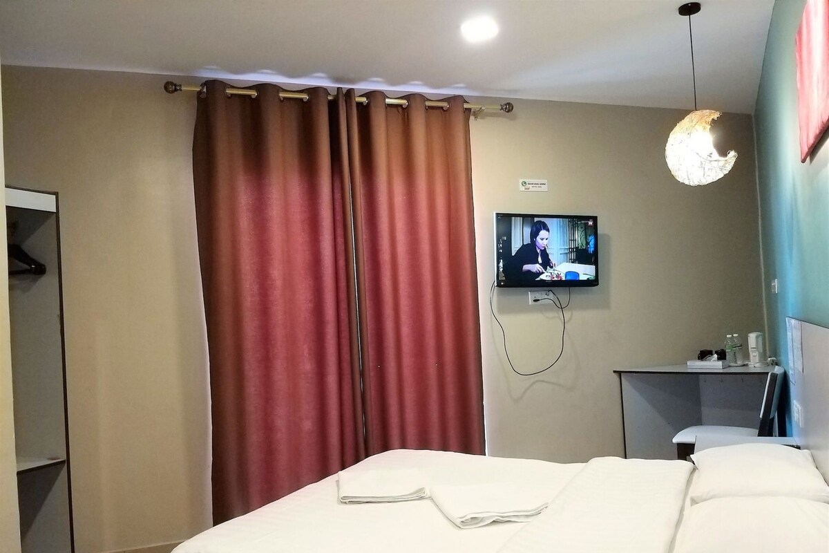 Ein Hotelzimmer mit einem Bett, einem an der Wand befestigten Fernseher, einem Schreibtisch mit Stuhl und einem Kleiderschrank.