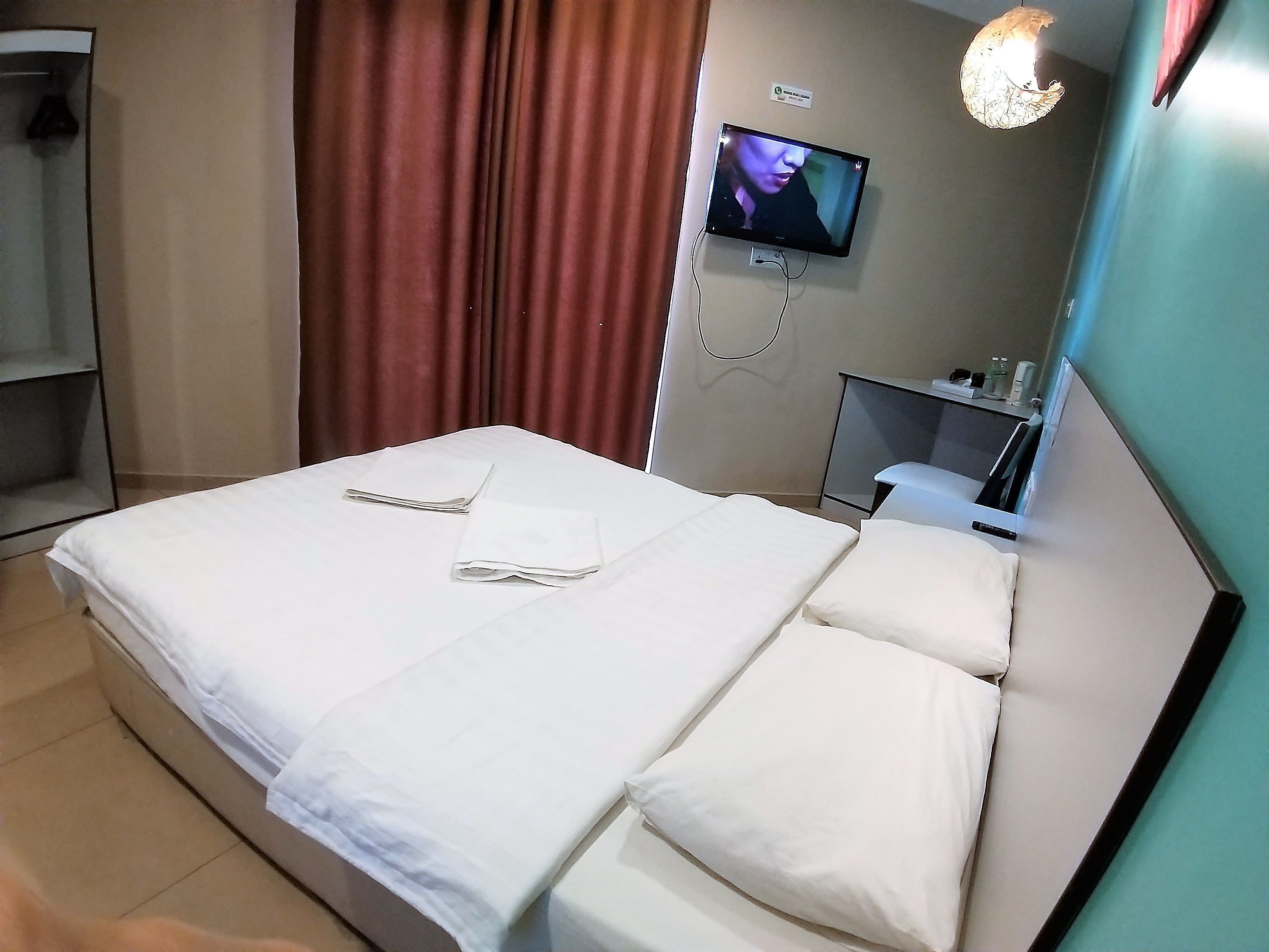 A hotel room with a bed, a TV mounted on the wall, and a small table with a chair.