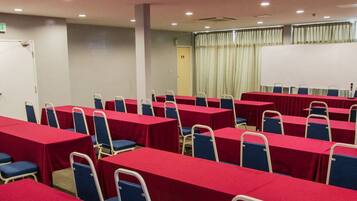 A conference room with rows of tables and chairs, a projector screen, and a door labeled "KELUARAN".