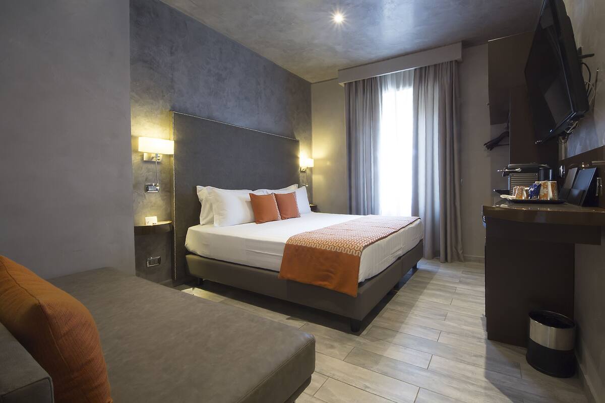 Una habitación de hotel moderna con una cama grande, lámparas de noche, un televisor de pantalla plana y un pequeño escritorio.