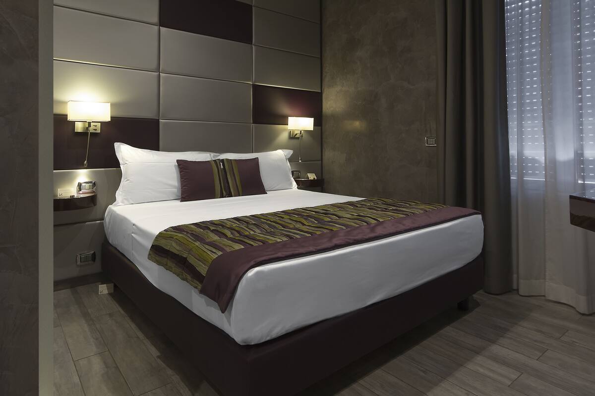 Una habitación de hotel moderna con una cama grande, dos mesitas de noche y un cabecero con iluminación integrada.