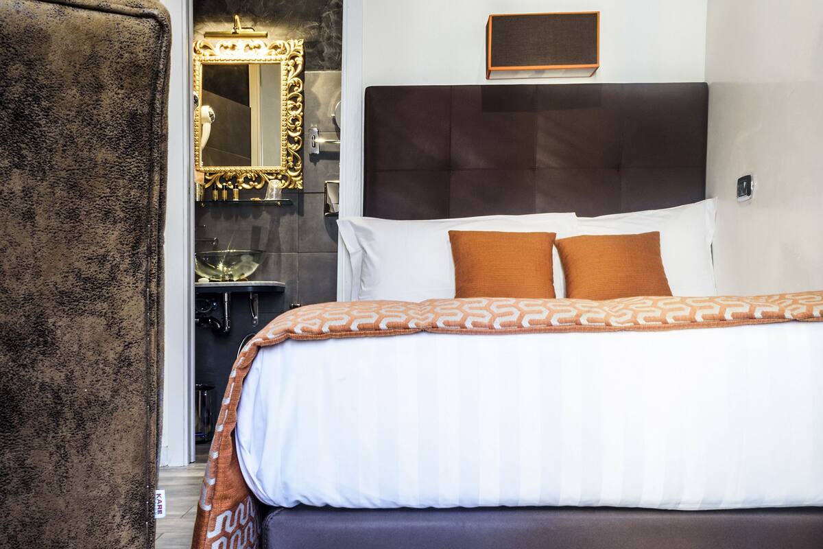 Una habitación de hotel moderna con una cama grande, un sillón cómodo y un espejo con un marco decorado.