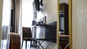 Una habitación de hotel con un espejo grande, un televisor montado en la pared, un escritorio con una silla y un armario.