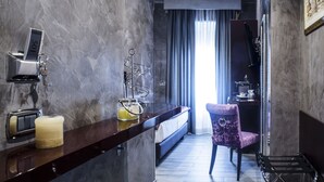 Una habitación de hotel moderna con pared de mármol, un minibar, una silla morada y una cama con vistas a la ciudad.