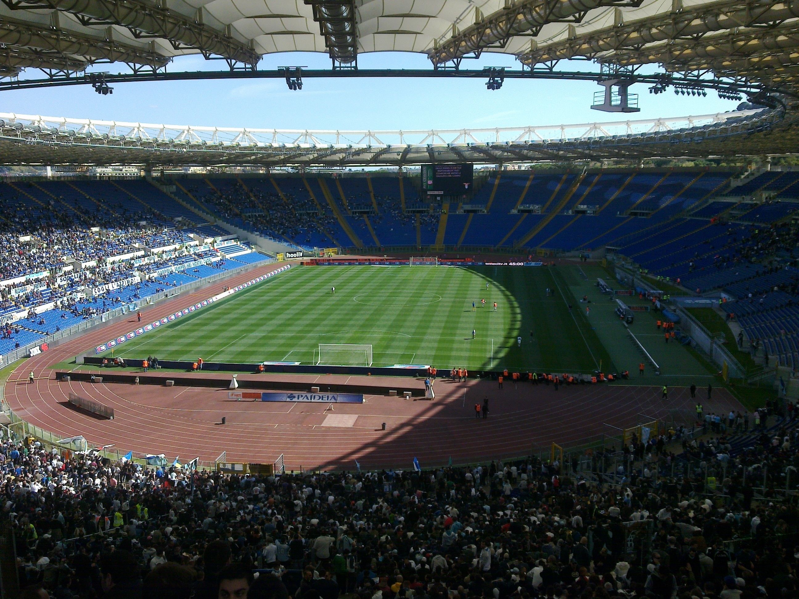 Un estadio con varios niveles de asientos, un campo central y una pista alrededor del campo.