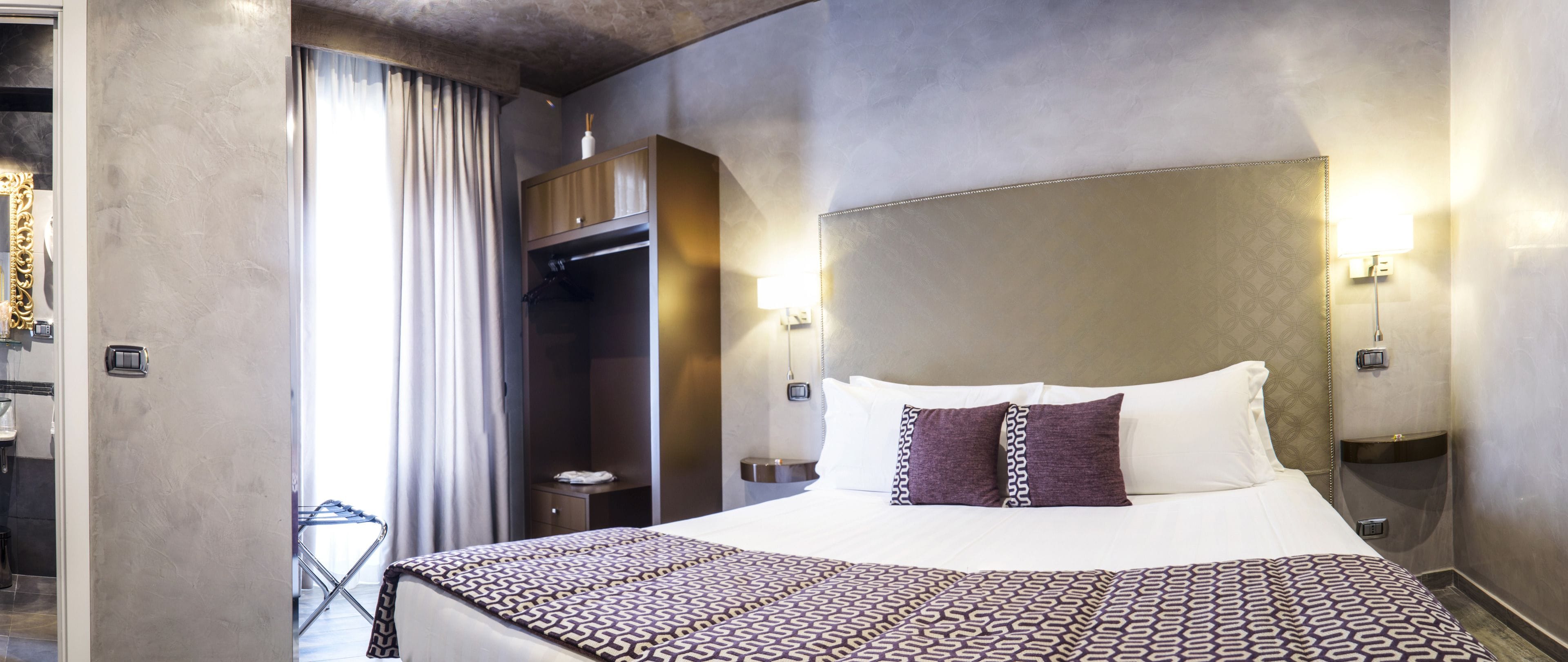 A hotel room with a large bed, a wardrobe, a bedside table, and a nightstand.