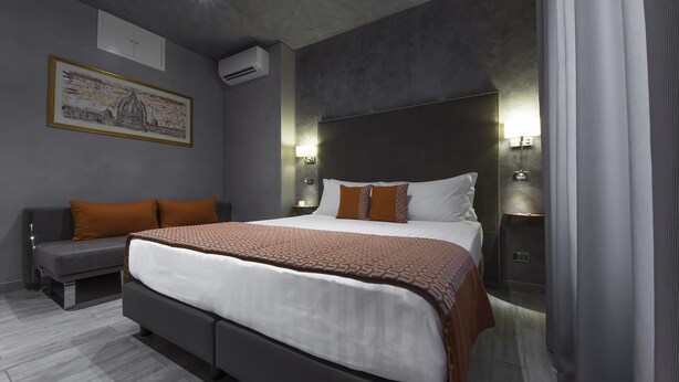 Una habitación de hotel moderna con una cama grande, un sofá y dos lámparas fijadas a la pared.