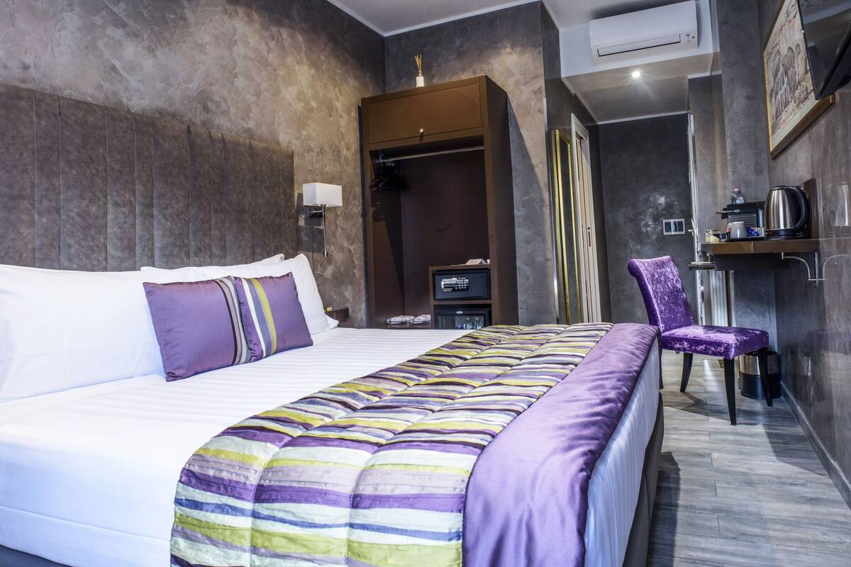 Una habitación de hotel moderna con una cama grande, una mesita de noche, una silla y un armario.