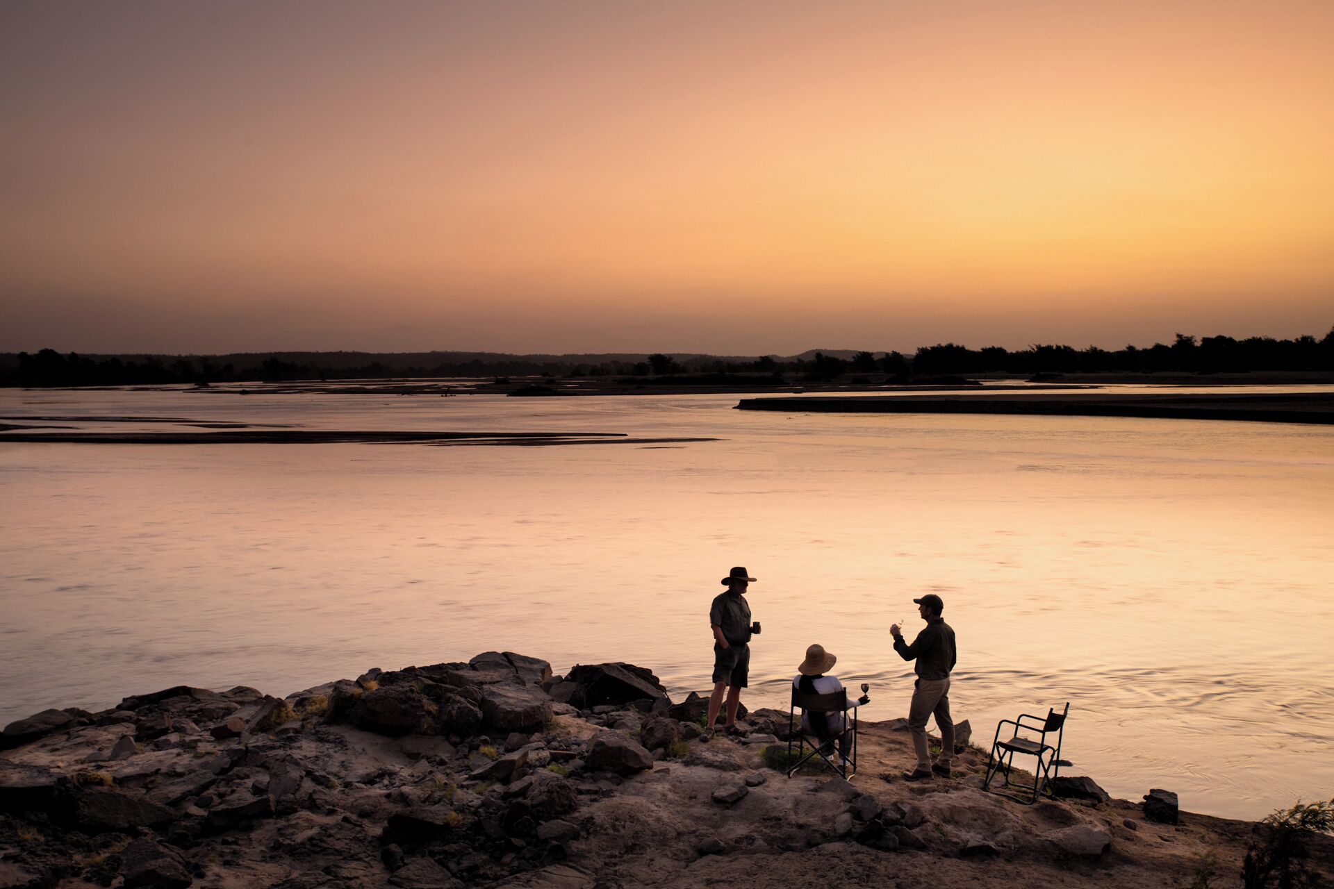 Un coucher de soleil sur une rivière paisible aux rives rocheuses.