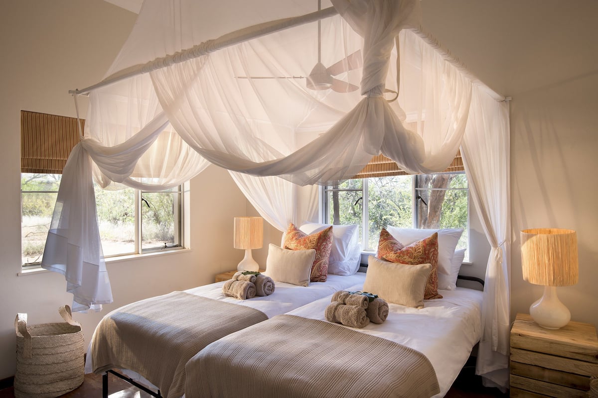 Une chambre avec un lit à baldaquin, deux tables de chevet, une lampe et une vue sur l’extérieur.