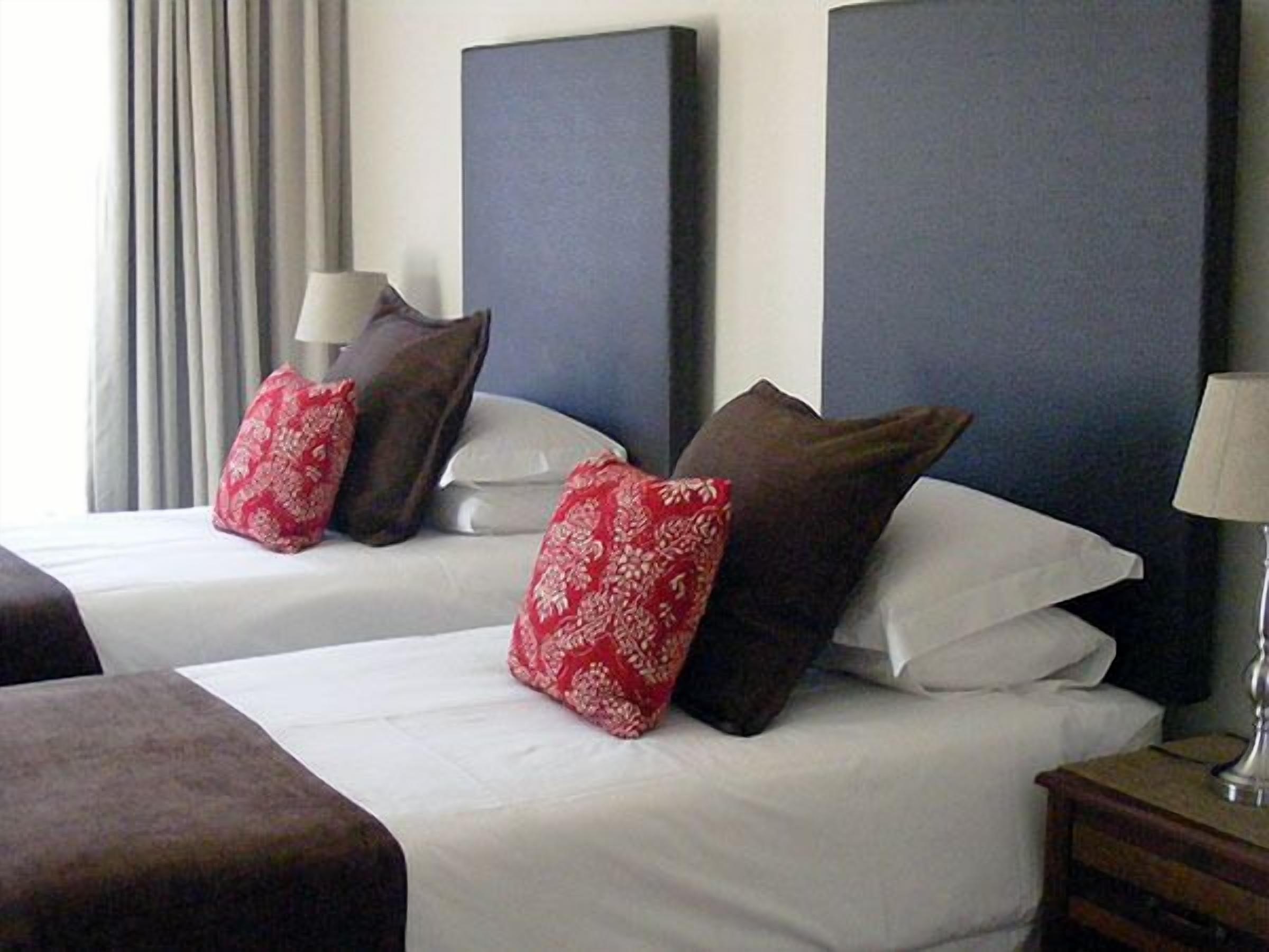 A hotel room with two beds, each with white linens and decorative pillows. There is a nightstand with a lamp on the right side.