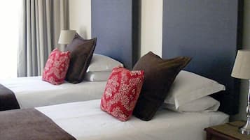A hotel room with two beds, each with white linens and decorative pillows. There is a nightstand with a lamp on the right side.