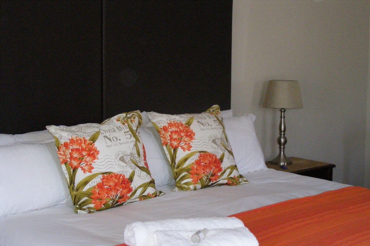 A neatly made bed with white linens, two decorative pillows with floral patterns, and a folded white towel on the bed.