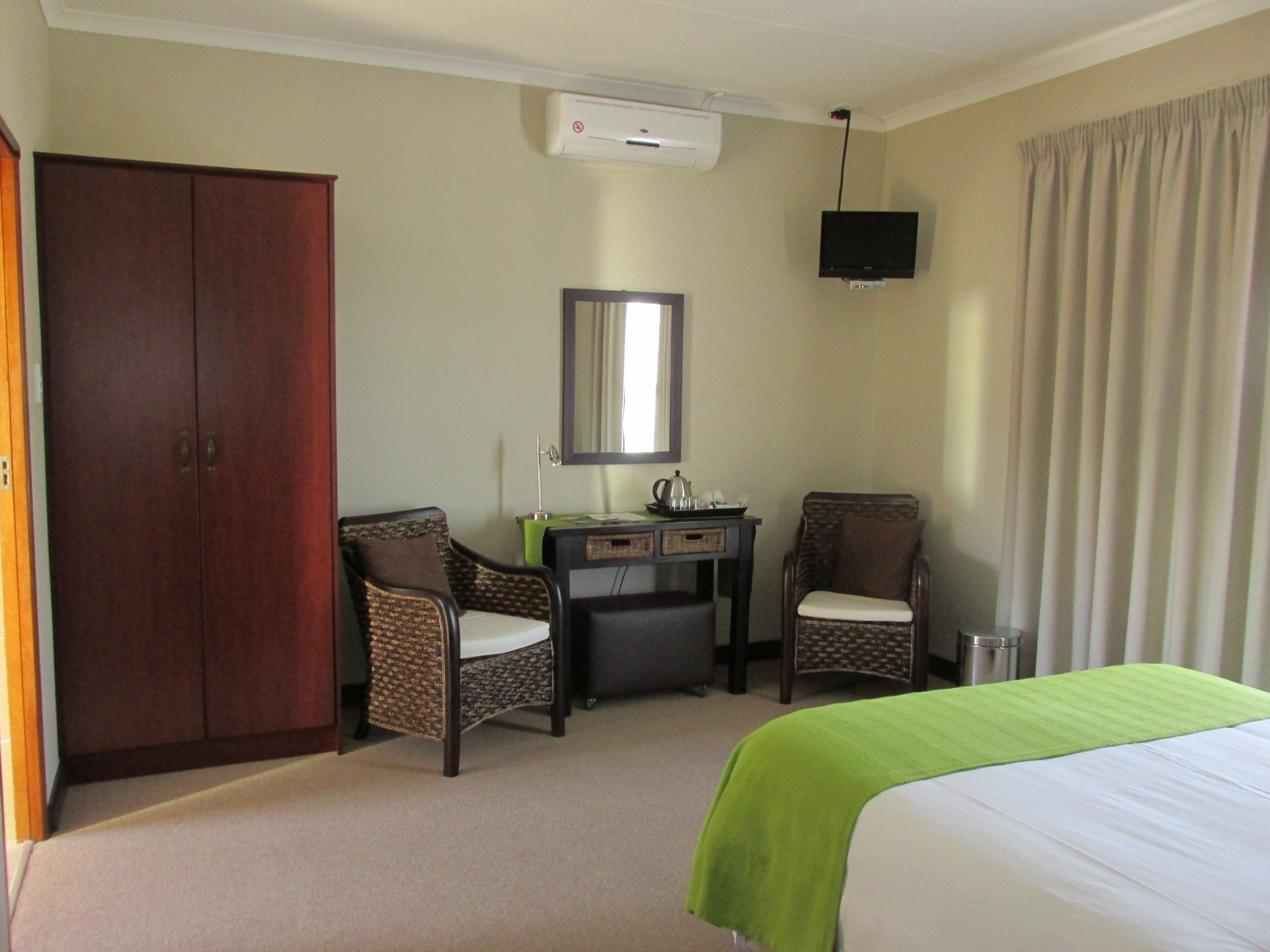 A hotel room with a bed, two chairs, a desk with a mirror, and an air conditioning unit.
