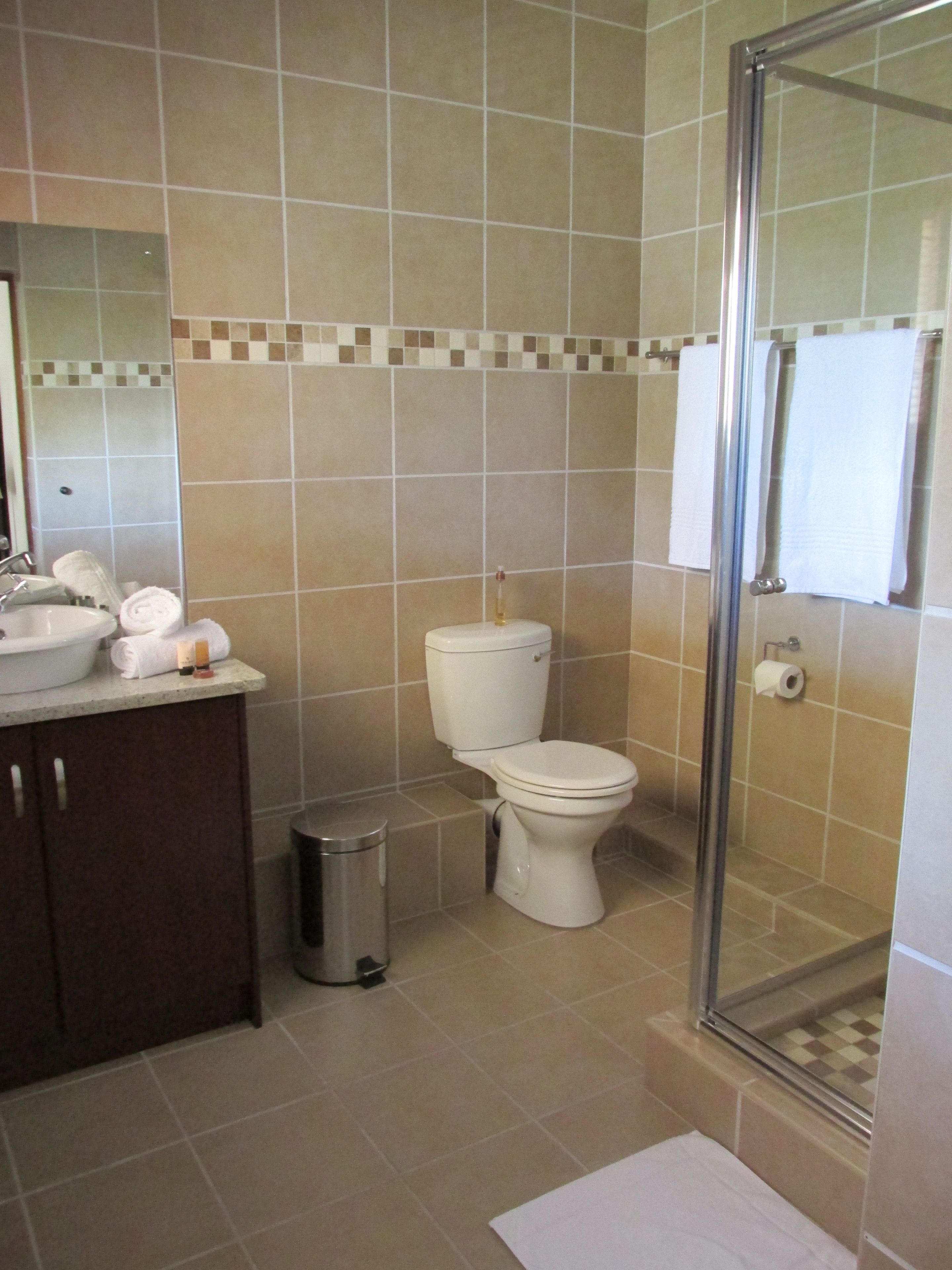 Ein Badezimmer mit Toilette, Waschbecken und Spiegel. Ein Mülleimer und eine Duschkabine sind ebenfalls vorhanden.