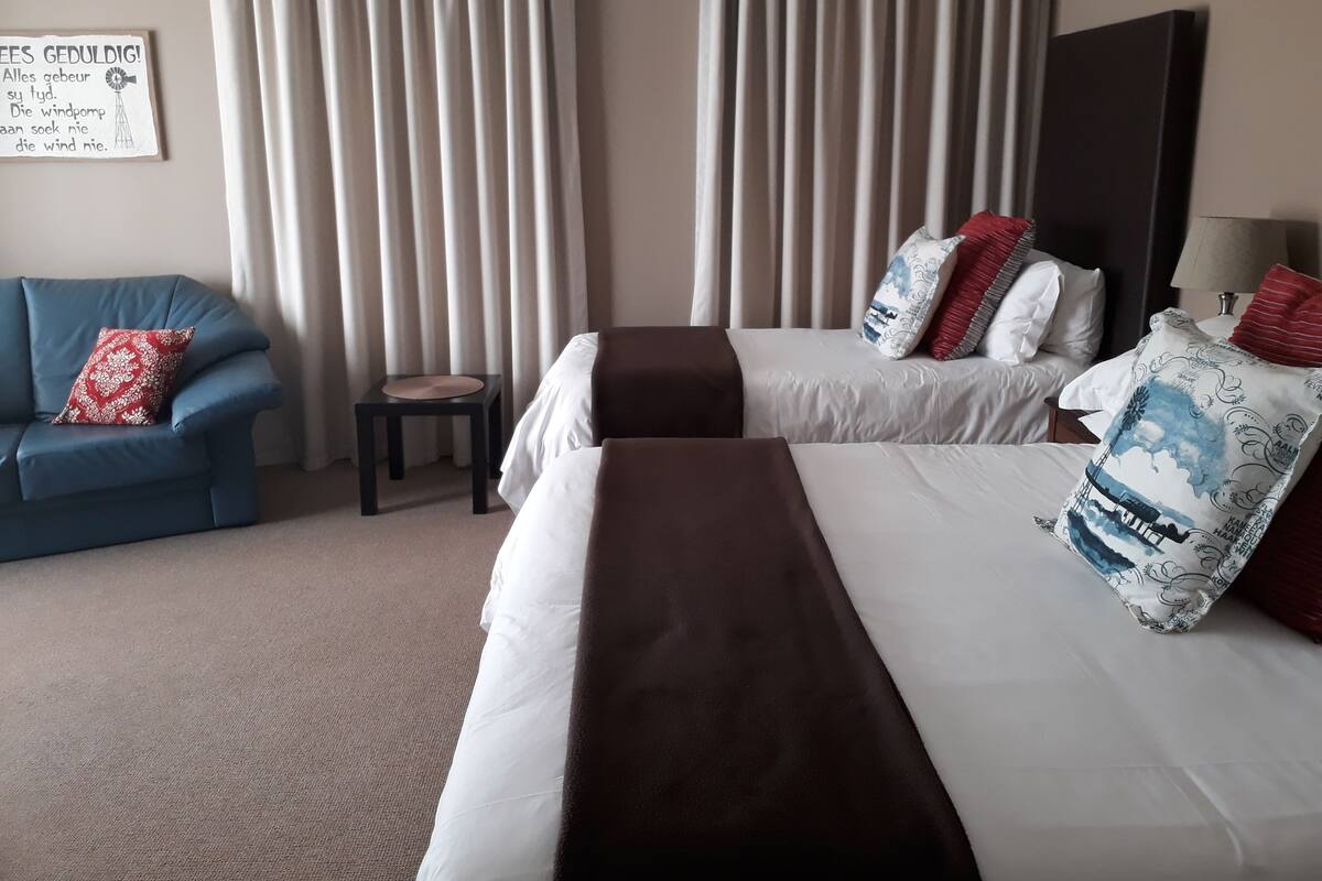 A hotel room with two beds, a blue sofa, and a small table.