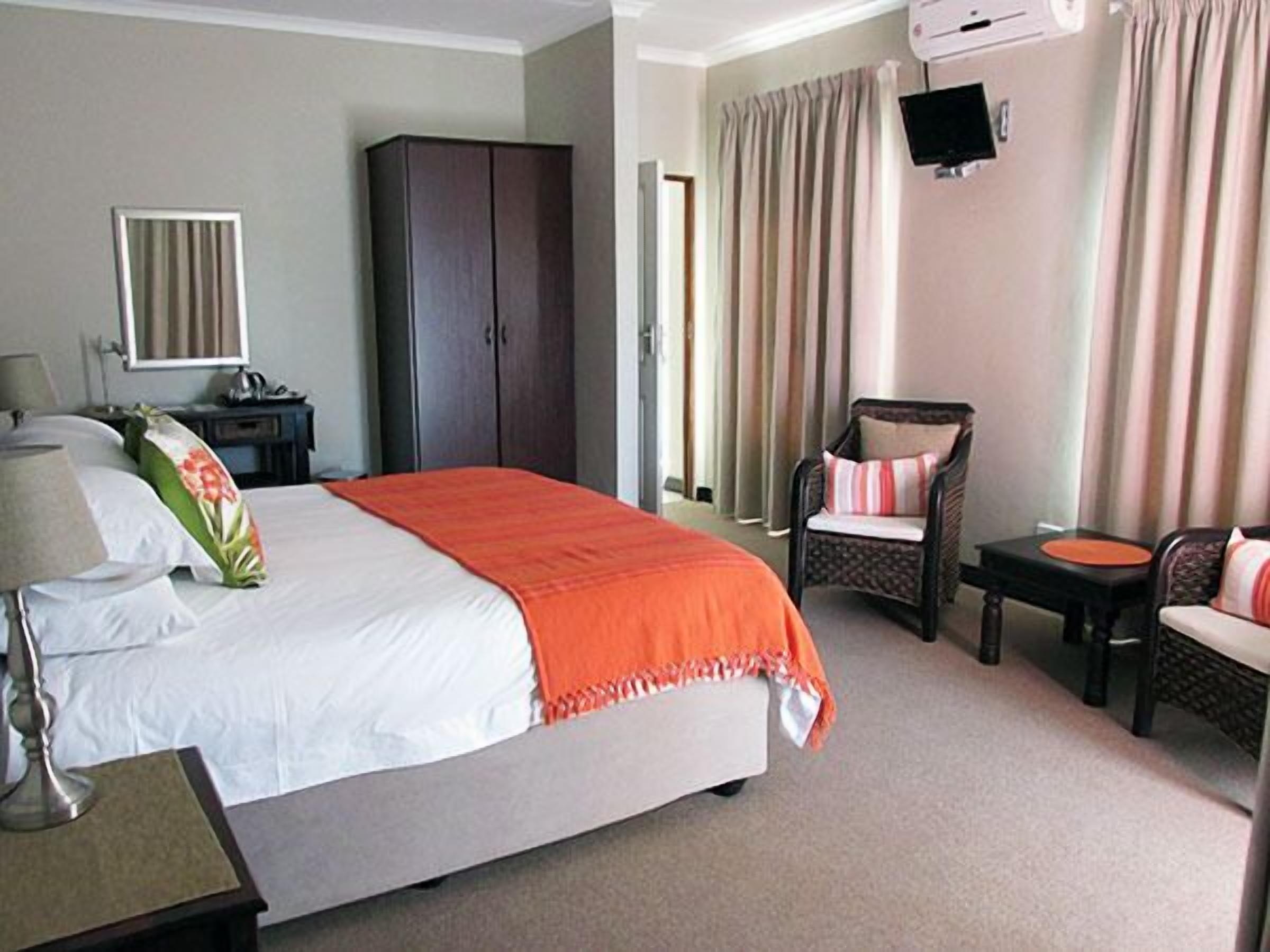 Una habitación de hotel con cama, una silla, escritorio, armario y televisor montado en la pared.