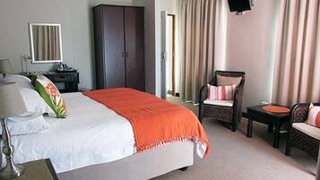 Una habitación de hotel con cama, una silla, escritorio, armario y televisor montado en la pared.