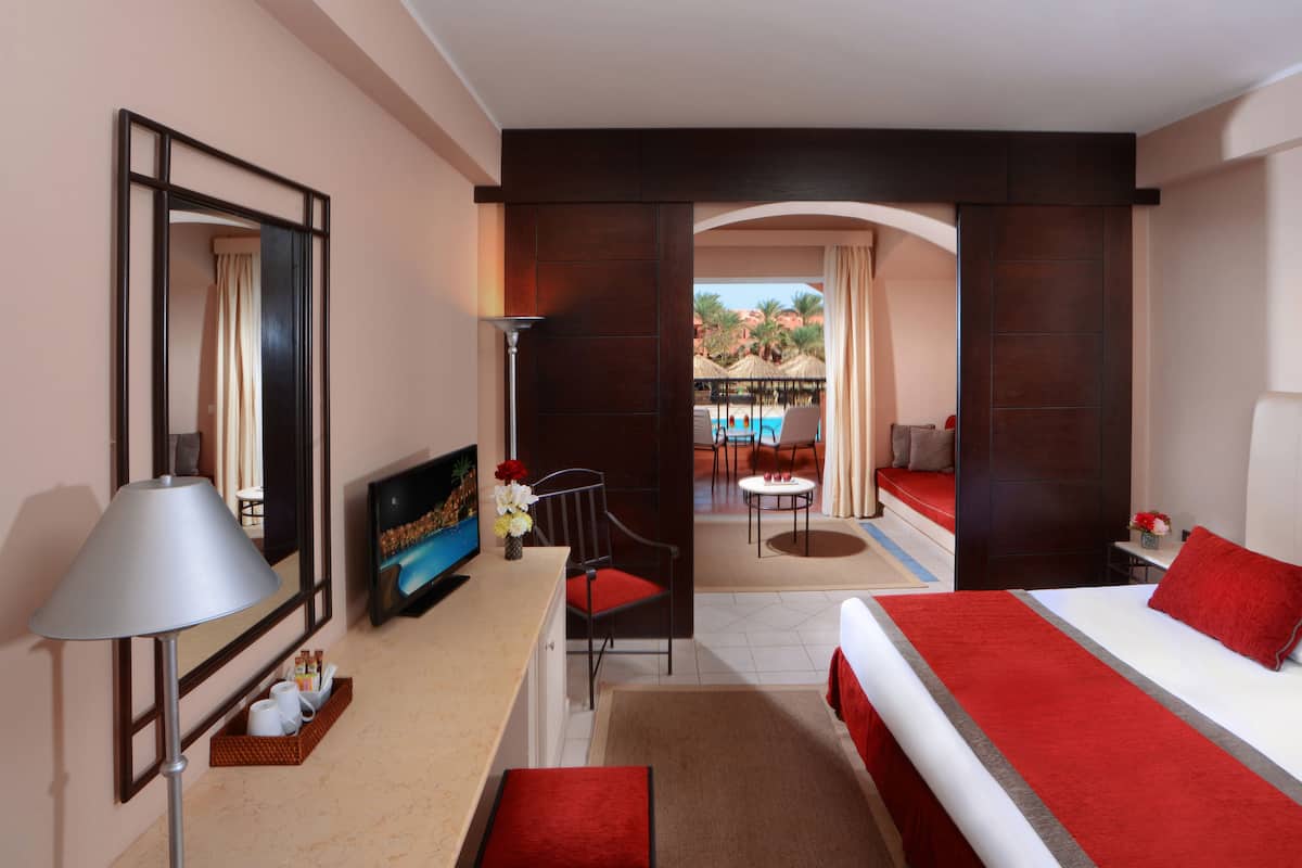 A hotel room with a bed, a desk, a chair, a TV, and a view of an outdoor pool area.