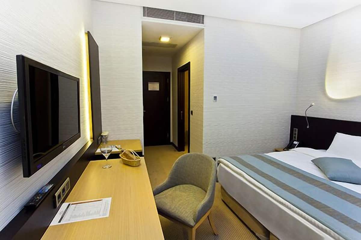 Ein Hotelzimmer mit einem Bett, einem Schreibtisch mit Fernseher, einem Sessel und einem Nachttisch.