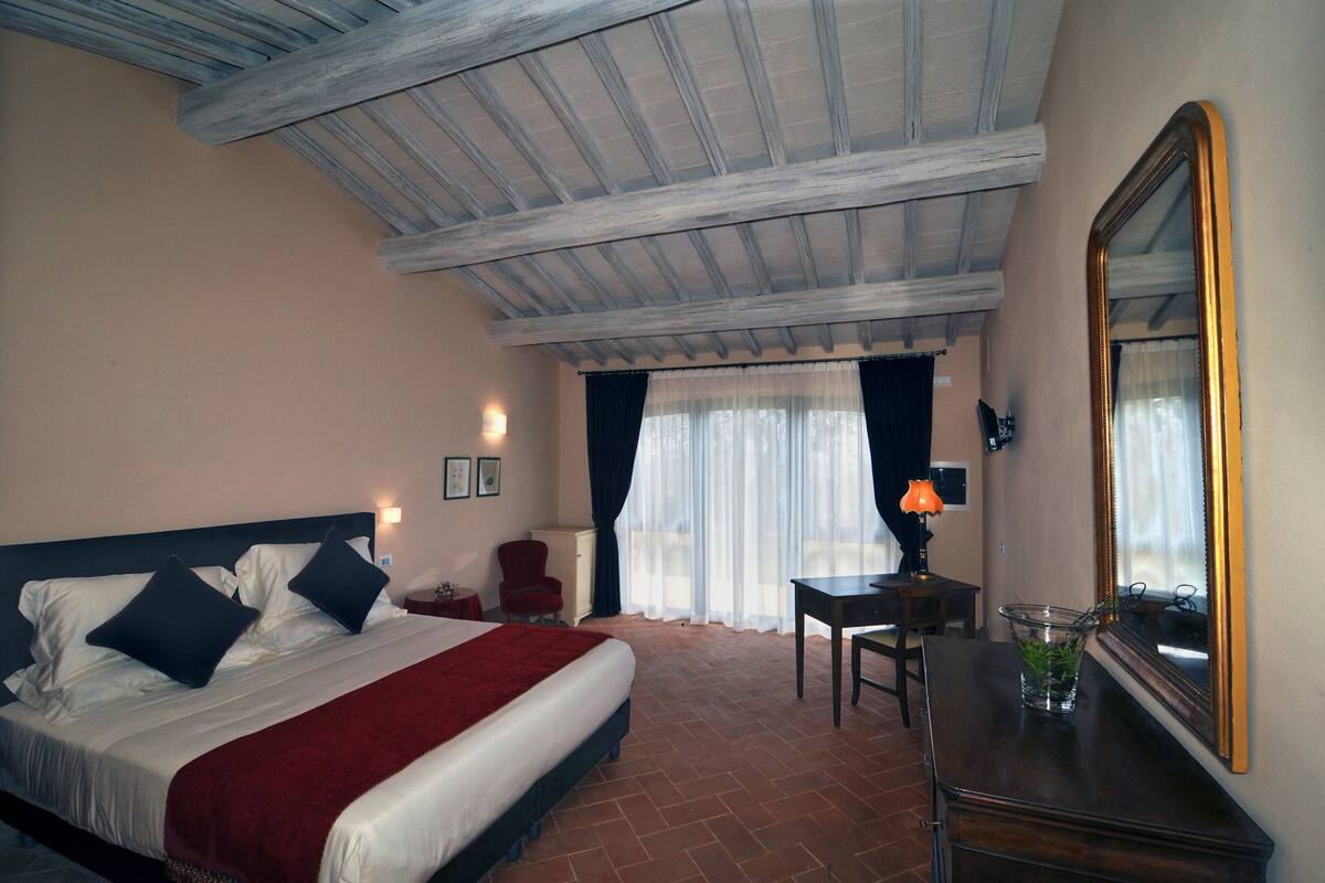 A hotel room with a bed, a desk, a chair, a mirror, and a window with curtains.