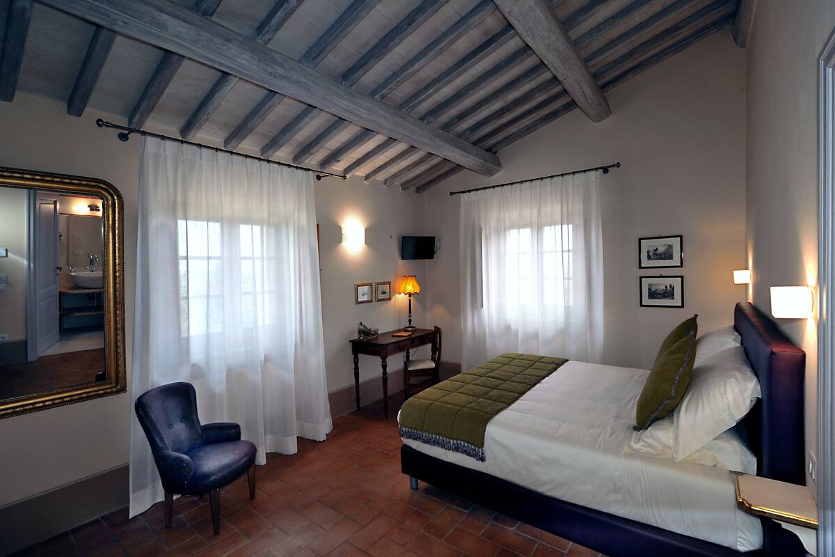 A bedroom with a bed, a chair, a desk, a mirror, and a television.