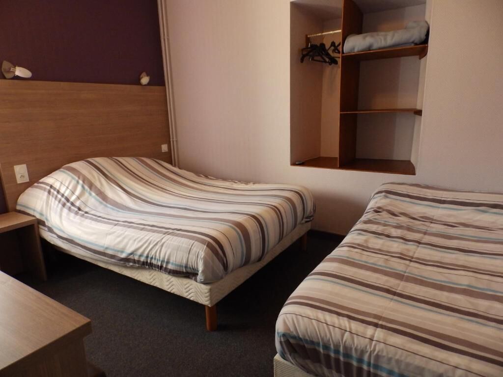 A room with two beds, a wooden headboard, a small table, and a built-in closet with shelves.