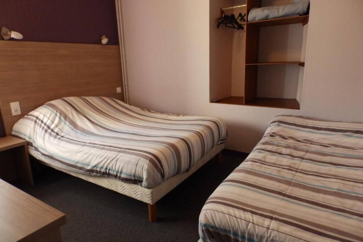 A room with two beds, a wooden headboard, a small table, and a built-in closet with shelves.