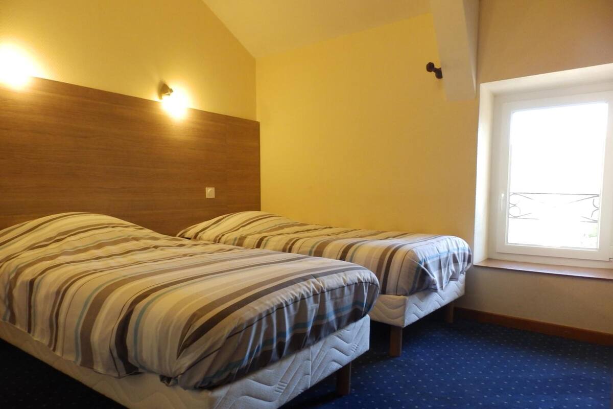 A bedroom with two beds, a wooden headboard, a window with a view, and a blue carpet.