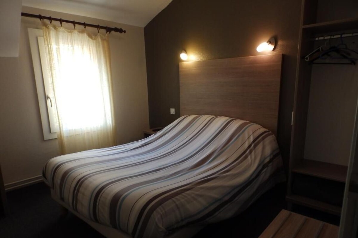 A bedroom with a bed, a window with curtains, a headboard with lights, and a wooden bench.