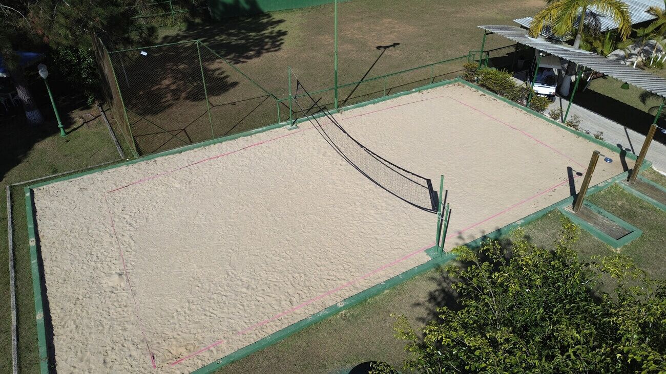 A volleyball court with a net, surrounded by a green fence and a small shelter.