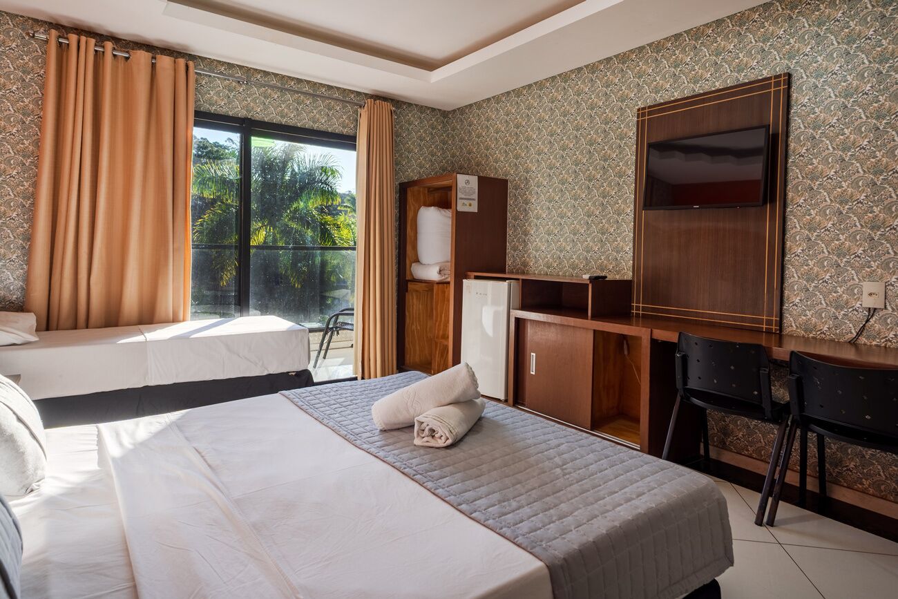 Ein Hotelzimmer mit Bett, Schreibtisch, Kleiderschrank und einem großen Fenster mit Vorhängen.