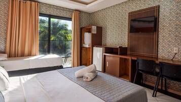 Ein Hotelzimmer mit Bett, Schreibtisch, Kleiderschrank und einem großen Fenster mit Vorhängen.