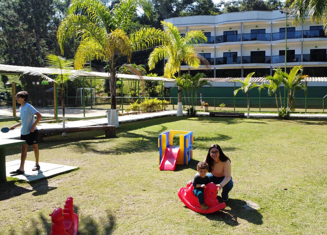 A playground with a slide and a climbing structure, surrounded by grass and palm trees.