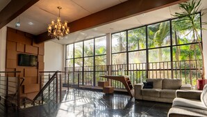 Eine geräumige Lobby mit hoher Decke, einer Chandelier, einer Treppe, einer Couch und großen Fenstern mit Blick auf Palmen.