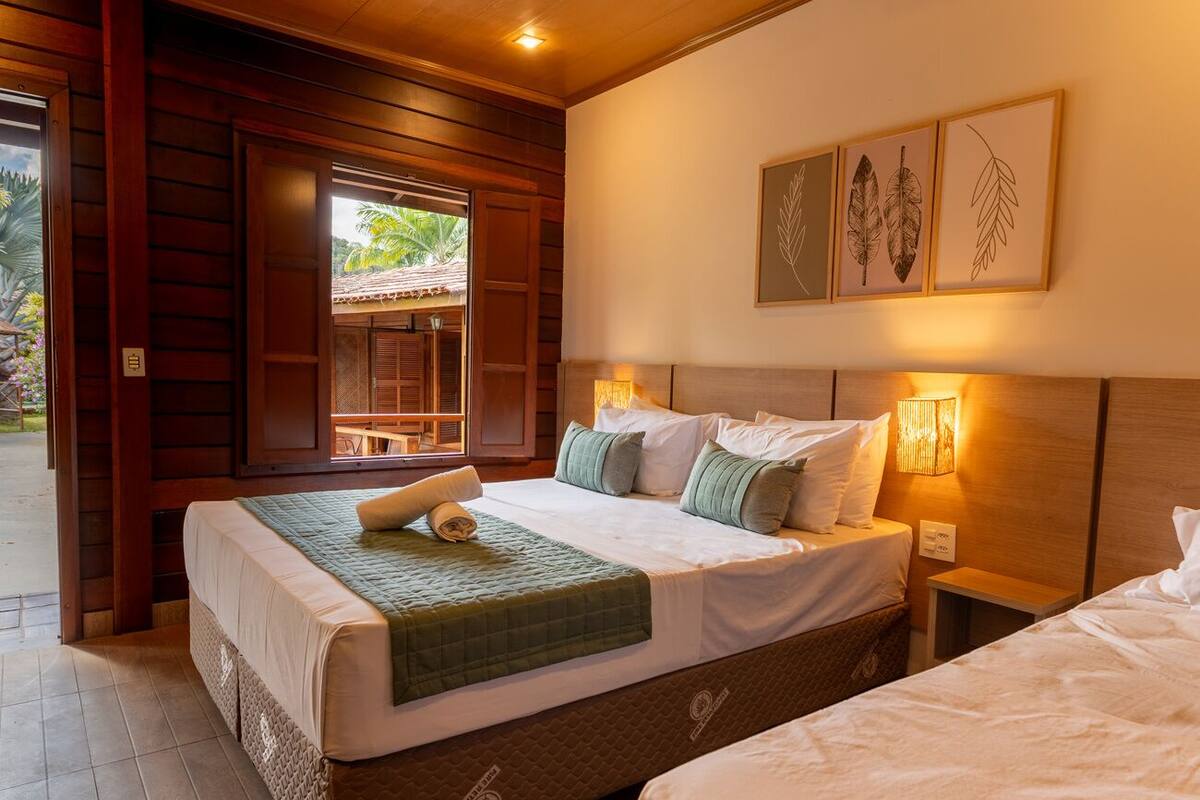 Habitación de hotel con una cama grande, cabecera de madera, mesita de noche pequeña y una lámpara fijada a la pared.