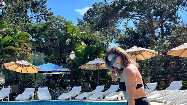 Ein Poolbereich mit Liegestühlen und Sonnenschirmen, umgeben von Bäumen und blauem Himmel.