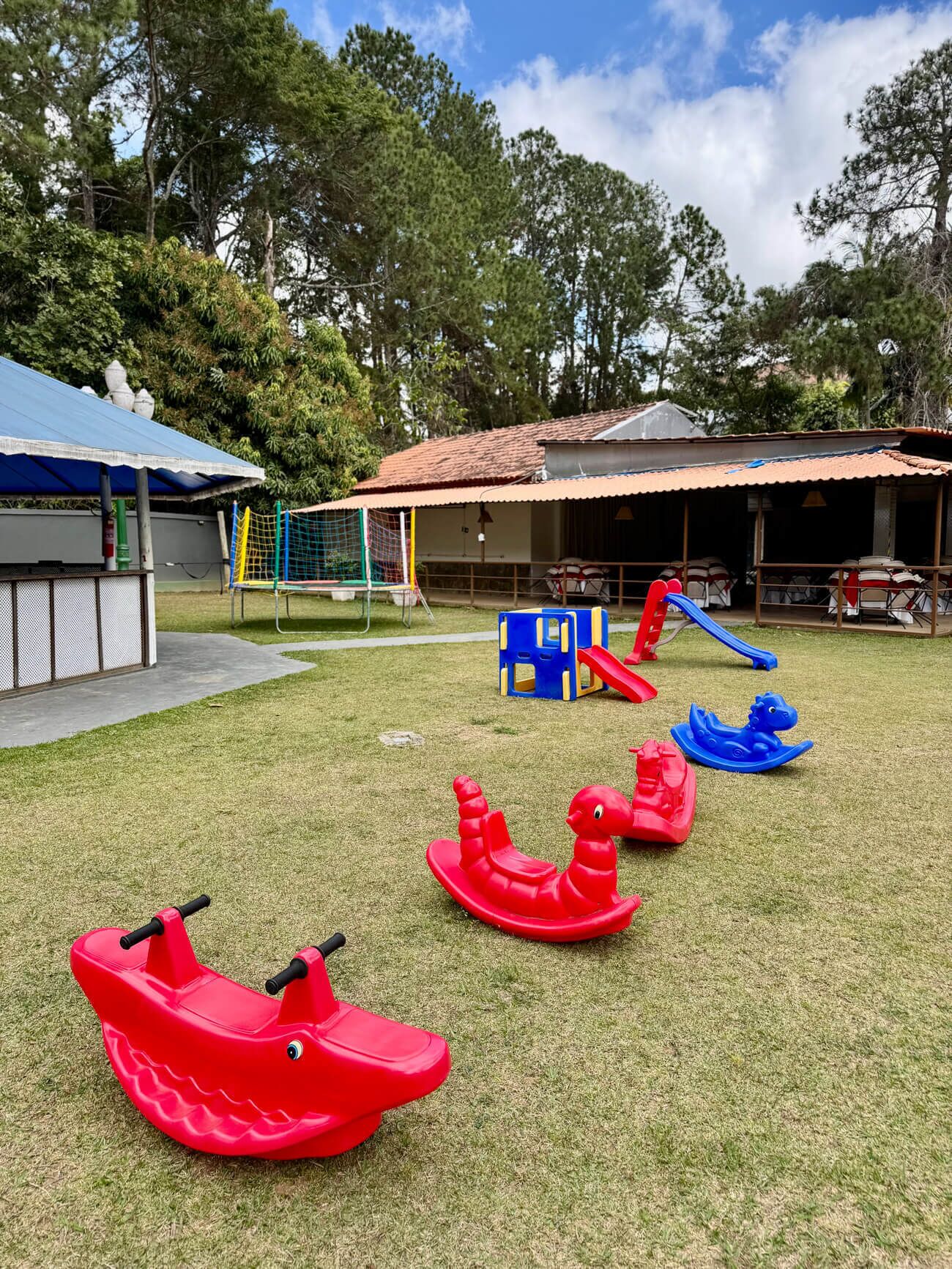 Um parquinho com brinquedos para andar, como carrinhos vermelhos e azuis, um gol de futebol e uma área de estar coberta.