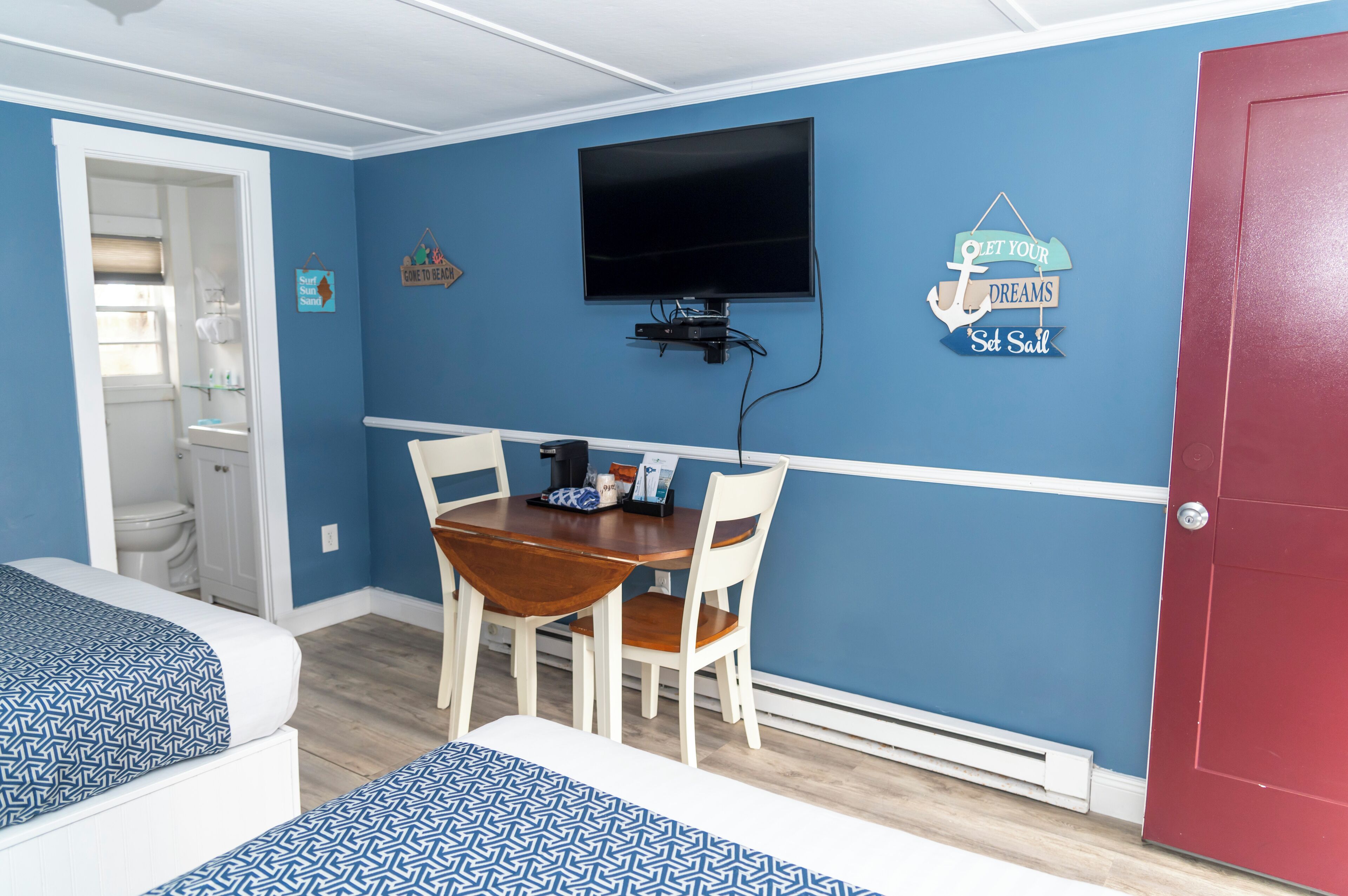 Une chambre avec deux lits, une table à manger avec des chaises, un téléviseur fixé au mur et une porte rouge.